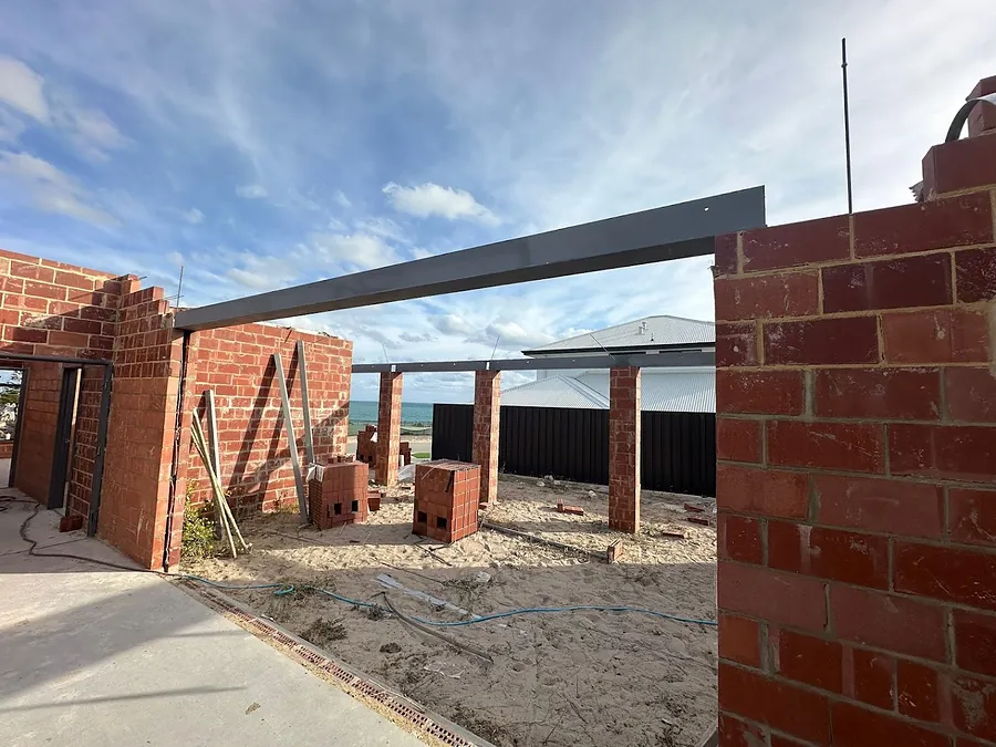 A charcoal steel lintel spanning brick piers on a coastal new build, with the ocean beyond
