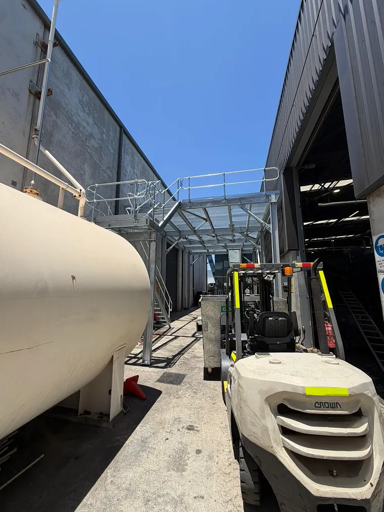 A galvanised steel mezzanine platform and walkway canopy frame installed in the laneway between two industrial units