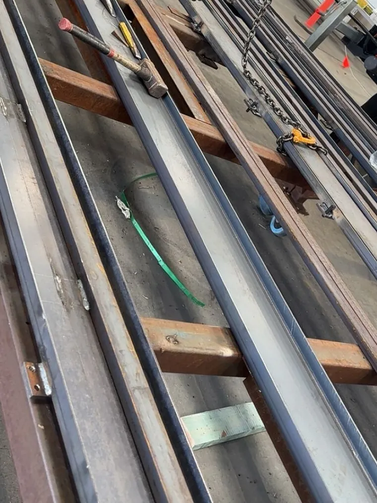 Long steel rails set out on trestles in the workshop with lifting chains rigged ready to move