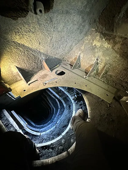 A gusseted steel billet ledge fitted over a chute opening in a confined space, lit by torchlight