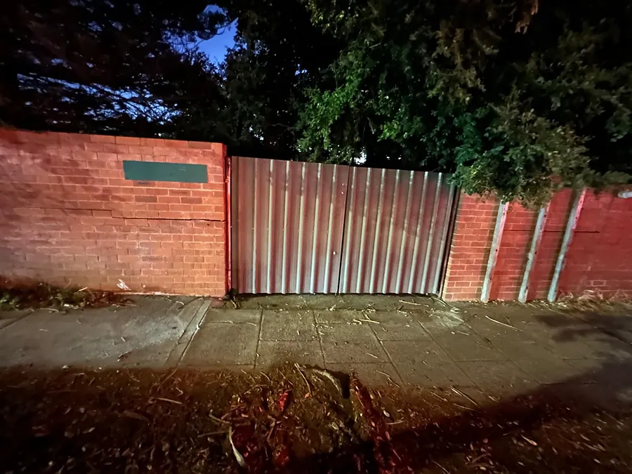 A sheeted steel gate and posts installed into a red brick boundary wall