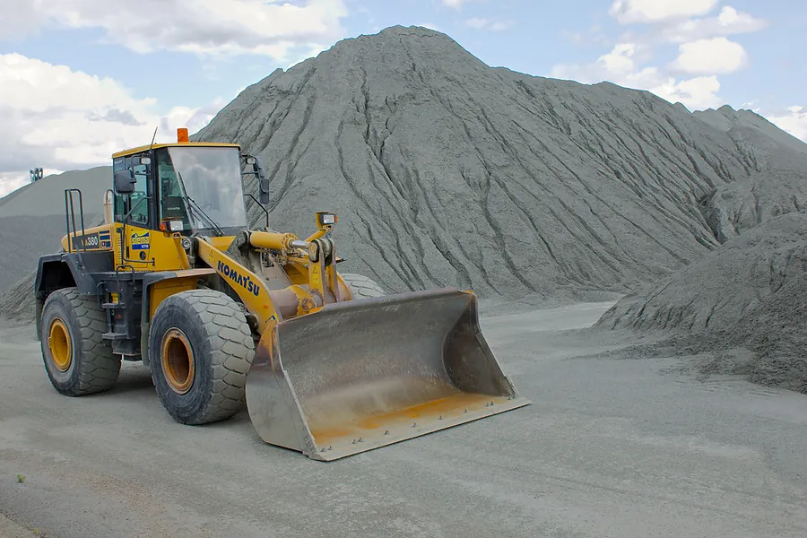 A wheel loader working a quarry stockpile, the cutting edge of its bucket worn back from use