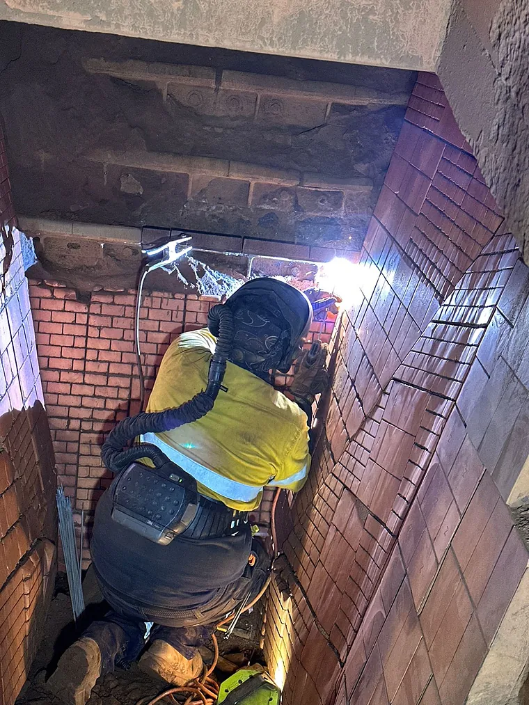 A Steel Point welder in hi-vis, welding helmet and powered air respirator welding steel reinforcement into a brick opening
