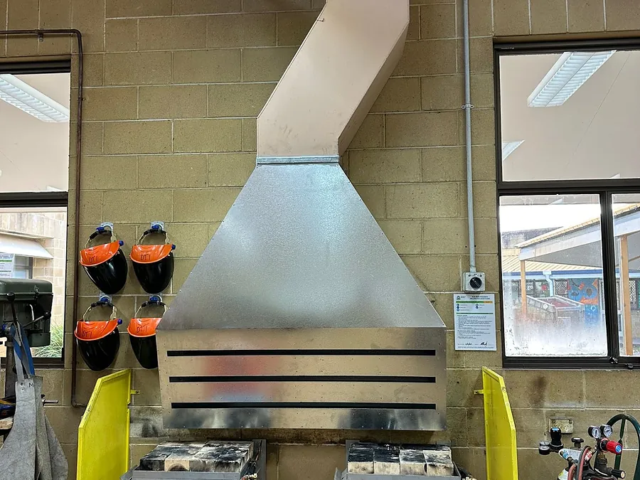 A fabricated galvanised fume extraction hood and ducting installed above the welding bays of a school metalwork workshop